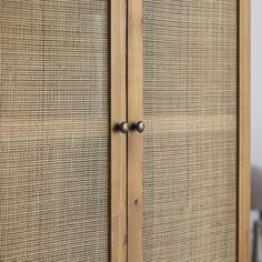 a wooden cabinet with metal handles and wicker panels on the doors, in front of a white wall