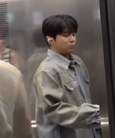 a young man wearing ear buds standing in front of a metal door with other people behind him