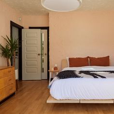 a bed sitting on top of a wooden floor next to a dresser and door in a bedroom