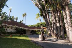 a woman is pulling her luggage down the street in front of palm trees and a house