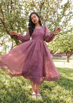 a woman standing in the grass wearing a purple dress