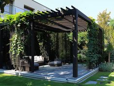 an outdoor living area with wooden pergols and green plants on the side of it