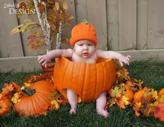 a baby in a pumpkin costume sitting on the grass with lots of leaves around him