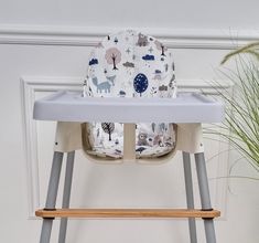 a baby high chair with a seat cover on it's back in front of a potted plant