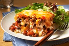 a white plate topped with lasagna next to a fork and green leafy salad