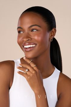 a smiling woman wearing two rings and a white top with her hand on her chest