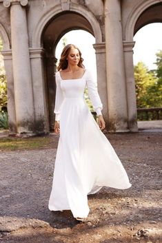 a woman in a long white dress is walking through an old stone building with arches