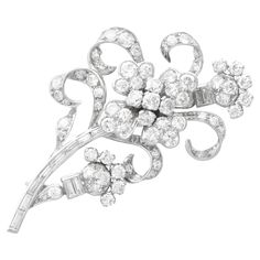 A stunning, fine and impressive antique 1920s 5.85 carat diamond and 15 karat white gold floral brooch; part of our diverse diamond flower brooches and jewellery collections. This fine and impressive antique diamond brooch has been crafted in 15k white gold. The diamond spray brooch is embellished with a central quatrefoil shaped design incorporating five individually claw set Old European cut diamonds in relief to four lobed petal designs, each embellished with four further pavé set diamonds. The elongated stem is comprised of nine channel set baguette cut diamonds, accented with scrolling leaf designs incorporating thirty-four pavé set Old European cut diamonds. This stunning brooch is further ornamented with two bud designs, each bearing a combination of Old European and baguette cut di Diamond Flower Brooch, Plant Jewelry, Floral Brooch, Brooch Bouquets, Diamond Brooch, Baguette Cut Diamond, Gold Brooches, Diamond Flower, European Cut Diamonds