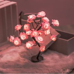 there is a small tree with pink roses on it in front of a box and other items