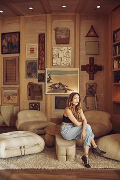 a woman sitting on top of a ottoman in a living room filled with furniture and decor