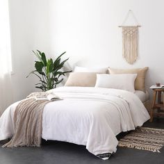 a bed with white sheets and pillows next to a potted plant on the floor