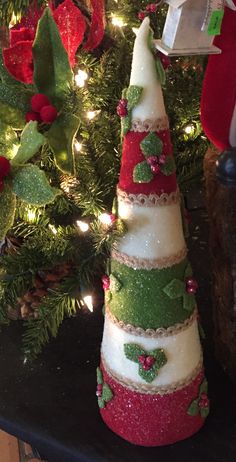 two small christmas trees are sitting on a table next to a tree with red, green and white decorations