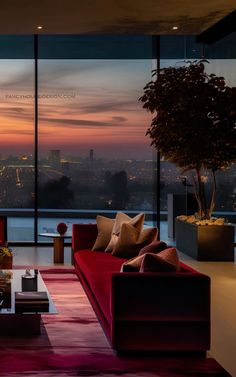 a living room with red couches and large windows overlooking the city at sunset or dawn