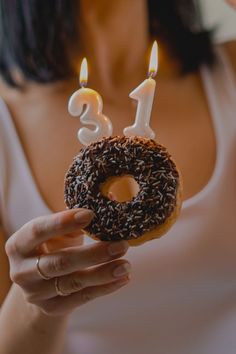 a woman holding up a donut with candles in the shape of number one on it