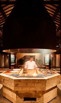 a man standing in front of a pizza oven on top of a wooden table next to a fire pit