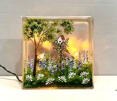 a glass block with a painting of a girl in the woods surrounded by flowers and trees