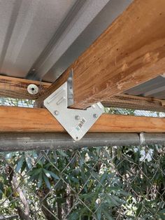 a close up of a metal and wood beam on a chain link fence with trees in the background