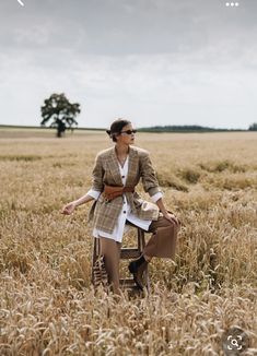 a woman standing in a wheat field with her hand on the back of a chair