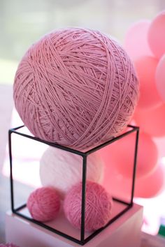 pink balls of yarn sitting on top of a black and white cubed container with balloons in the background