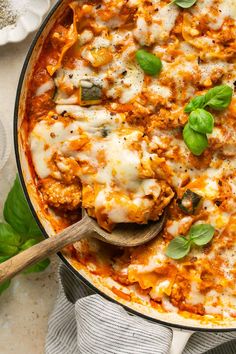 a casserole dish with cheese and spinach on the side next to a wooden spoon