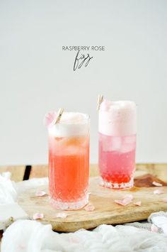 two drinks sitting on top of a wooden cutting board next to each other with pink and red liquid in them