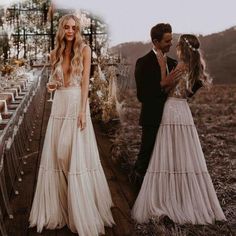 two people standing next to each other in front of a wooden walkway with white flowers and greenery