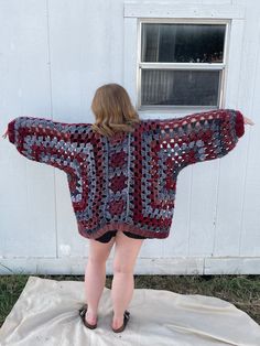 a woman standing in front of a white building wearing a red and blue crocheted sweater