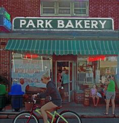 a woman riding a bike past a park bakery