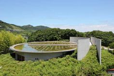 the circular building is surrounded by greenery and mountains in the distance, with trees surrounding it