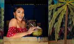 a woman in a red and white polka dot dress holding a coconut with a straw