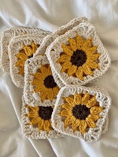 four crocheted coasters with yellow and brown sunflowers on them sitting on a white sheet