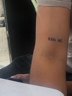 a person with a tattoo on their arm that reads kiss me and sits in front of an open laptop