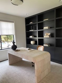 a room with a table, chairs and shelves filled with bookshelves next to a window