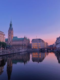 the city is lit up at dusk by the water's edge and buildings are reflected in the water