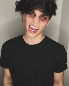 a young man with blood on his face and black t - shirt is standing in front of a white wall