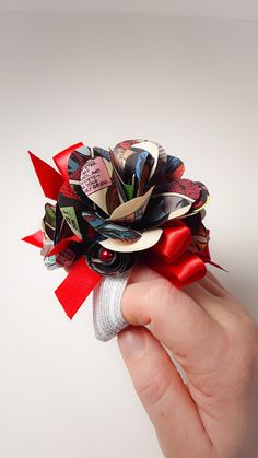 a hand holding a red and black flower made out of old magazine pages on it