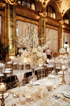 an elegant centerpiece with white flowers and candles sits on a table in a ballroom