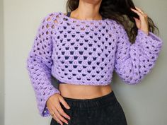 a woman wearing a purple crochet sweater and black shorts with her hands on her hips