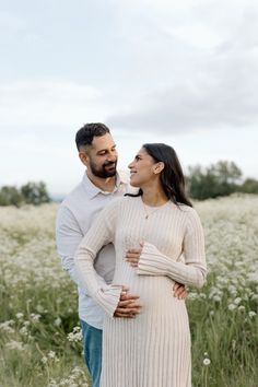 a pregnant couple standing in a field with tall grass