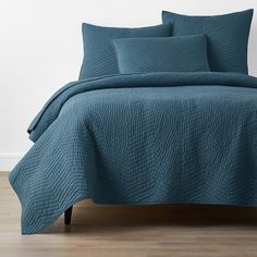 a blue quilted bedspread and pillows on a bed with wood flooring