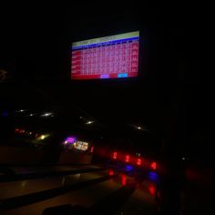 a bowling alley at night with neon lights on the floor and a large screen displaying numbers