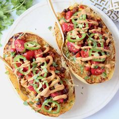 two stuffed sweet potatoes topped with toppings on a white plate next to a fork