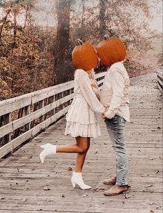 two people with pumpkins on their heads standing on a bridge in the woods by some trees