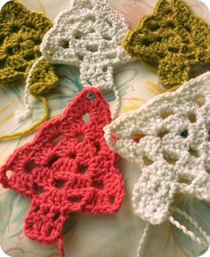 four crocheted items are laying on top of a floral print sheet, one is red and the other is white