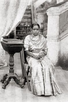 an old black and white photo of a woman sitting in a chair next to a table