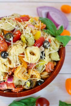 a wooden bowl filled with pasta salad on top of a white table next to vegetables