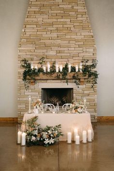 a table with candles and flowers is set up in front of a brick fire place