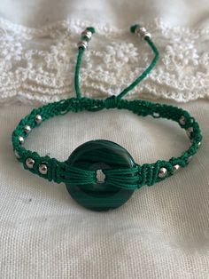 a green beaded bracelet sitting on top of a white cloth covered tablecloth next to a button