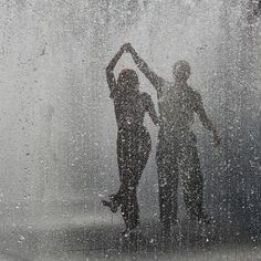 two people standing in the rain with their hands up to their heads and arms behind them