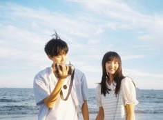 two people standing on the beach taking pictures